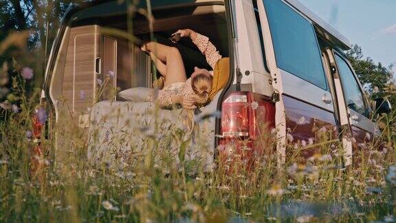 一名女子躺在一辆停在草地中央的露营车里使用智能手机