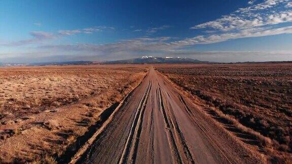 前进无人机拍摄的消失点土路与山脉的背景摩押外犹他州与沙漠平原在蓝天下的日落日出