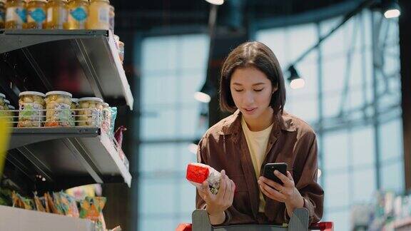 女人看着智能手机上的清单从货架上取下产品