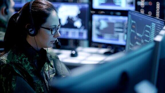 女军事技术支持专业人员给耳机指令她在一间有很多工作屏幕的监控室里