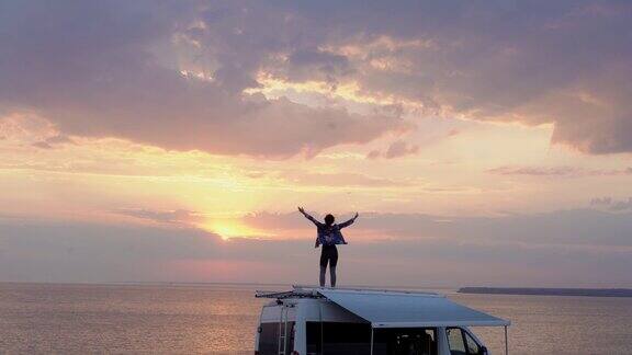 日落时分一个女人在海边露营车的屋顶上跳舞