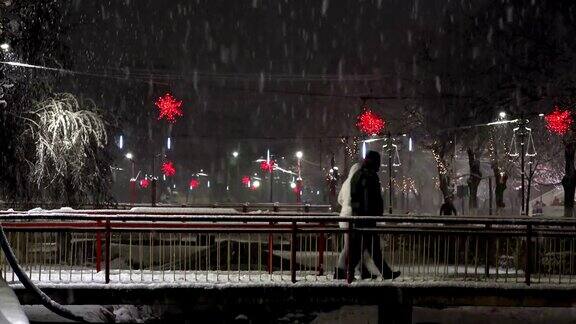 城市的圣诞景象人们在晚上的雪暴风雪过桥