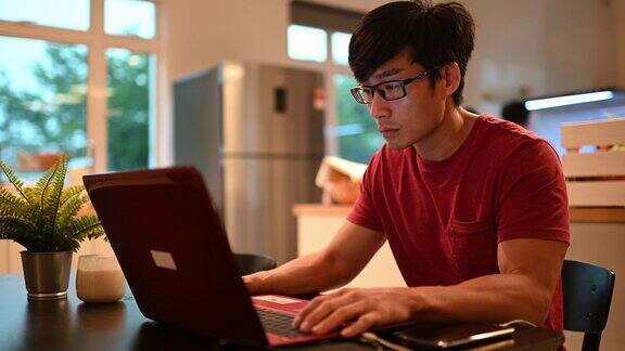一位亚洲华人中年人在餐厅吃早餐同时用笔记本电脑回复电子邮件