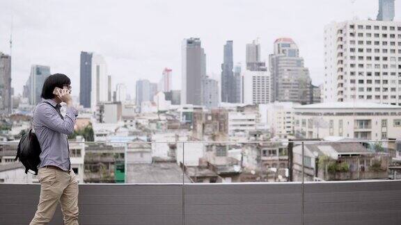 年轻的亚洲商人用智能手机在写字楼屋顶平台上谈生意背景是城市景色商务沟通和企业理念