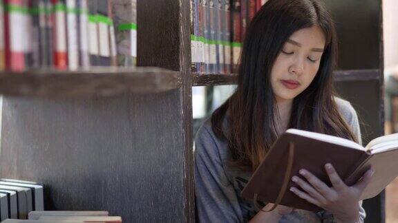 亚洲女学生坐在书架前在大学图书馆看书教育