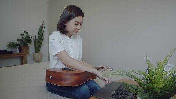 年轻女子一边玩原声吉他一边用笔记本电脑视频聊天