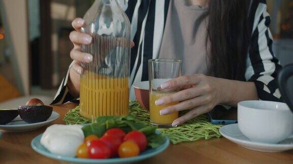 在家里吃早餐的时候女人用手往杯子里倒果汁喝