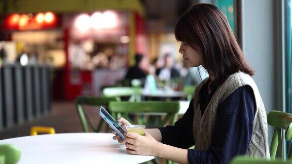 年轻漂亮的亚洲女人在酒吧一边喝着软饮料一边看她的智能手机