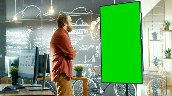 男性应用开发者看着带有绿色屏幕模型的交互式白板他在思考解决问题的方法在背景创意办公室与黑板墙与项目计划绘制
