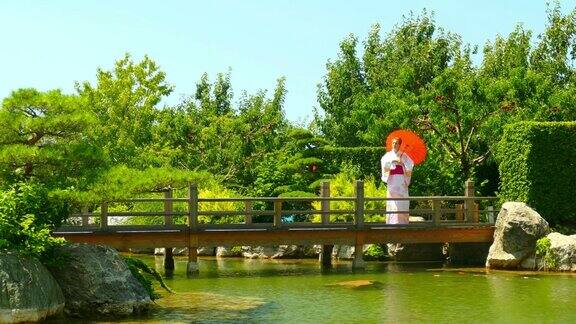 在一个绿色的公园里一个女人穿着和服带着一把伞站在河上的桥上