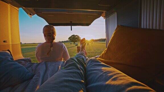 POV一个阳光明媚的日子一个男人躺在小木屋里一个女人坐在停在乡间某处的露营车前