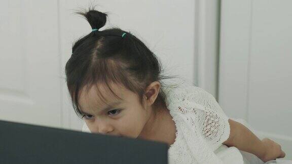 泰国小女孩正在她白色的房间里用笔记本电脑看卡通片