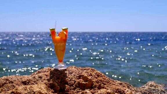 埃及海滩上的热带新鲜果汁与吸管站在海边的岩石上