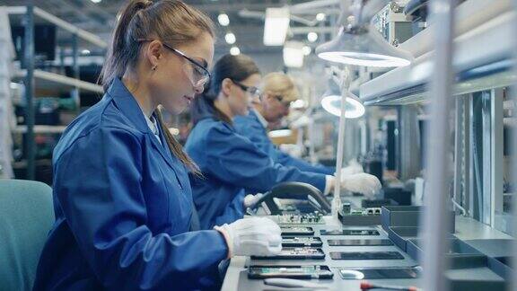 身穿蓝色工作服、戴着防护眼镜的电子厂女工正在用镊子组装智能手机的印刷电路板拥有更多员工的高科技工厂