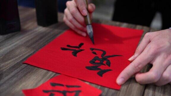 年轻的亚洲华人男性的手练习中国书法庆祝中国新年的家庭装饰目的与繁荣和良好的措辞写在一张红色的纸上
