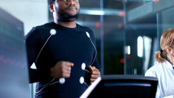 男性运动员在跑步机上跑步电极附在他的身体而运动科学家监督读取心电图状态拥有高科技设备的后台实验室