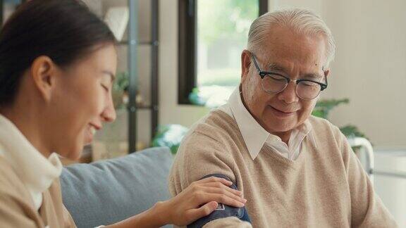 特写亚洲女性专业个人护理人员照顾老年男性使用血压计检查血压监测器在家里的沙发