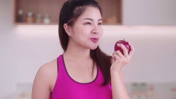 运动的年轻亚洲女性穿着运动服在厨房内吃苹果享受吃水果的饮食和健康的运动减肥概念
