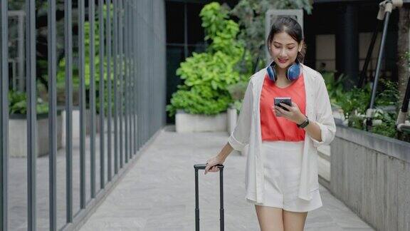 亚洲女商人拖着行李在机场候机楼的走廊上上班旅行时用你的智能手机交流无线通信技术