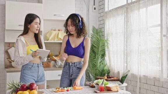 一名亚洲少女戴着耳机听着音乐用水果刀和朋友们在厨房里做蔬菜沙拉快乐地生活在一起烹饪娱乐生活中很少奢侈