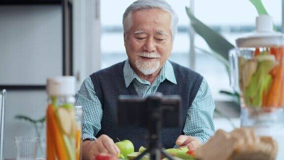 亚洲老年男性视频博客在手机上教烹饪老厨师是一名男性老人他在自己的视频博客上用手机录制了一个关于如何在家制作健康沙拉的视频教程