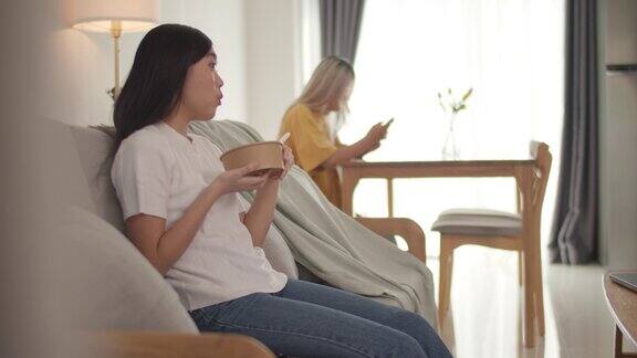 可爱的女性坐在沙发上吃蔬菜沙拉同时在家里看电视