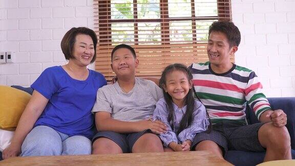 快乐的亚洲家庭坐在客厅的沙发上家庭放松和一起在家里度过时间看着相机