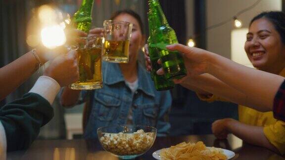 一群多民族年轻的亚洲朋友喝着酒啤酒瓶玻璃有乐趣的笑声享受聚会的夜生活在室内的家