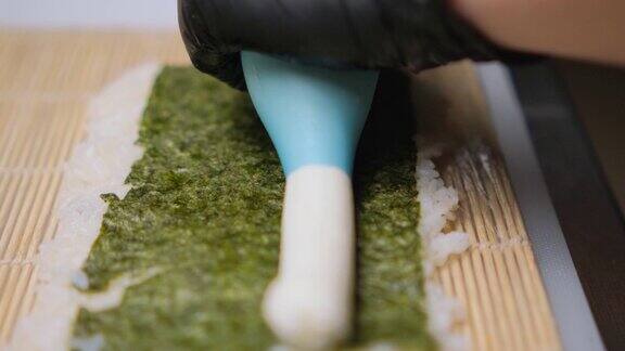 一位厨师在做寿司厨师把奶油奶酪挤在海苔和米饭上