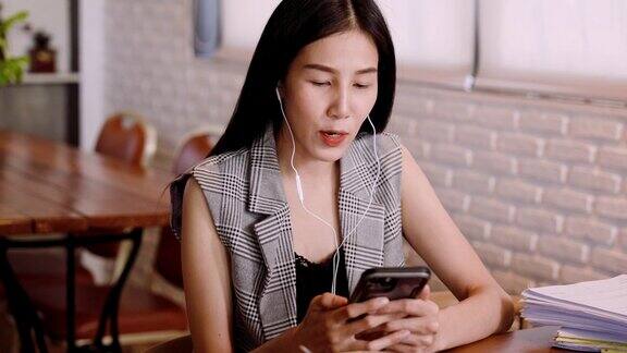 肖像亚洲女人手里拿着手机用耳机打电话给同事咨询工作解决方案坐在办公室外面的咖啡店里工作