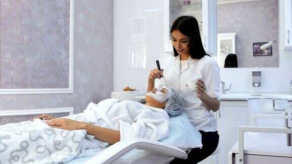 漂亮的美容师小心地将一个粘土面膜在一个年轻的女人在水疗中心