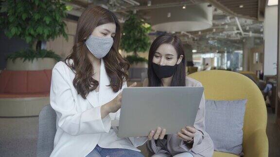 两位在办公室使用笔记本电脑开会的亚洲商务女性戴着医用口罩在办公室工作