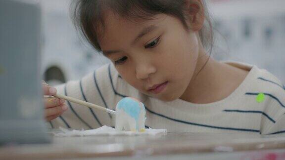 亚洲小女孩的慢镜头在小陶瓷象上兴致勃勃地画着油画孩子们在学校的艺术和手工艺创意活动班