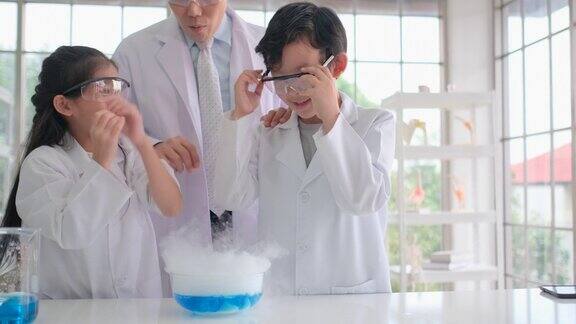 亚洲年轻的科学家男孩和女孩享受和乐趣与干冰实验通过倒蓝色的化学物质到干冰