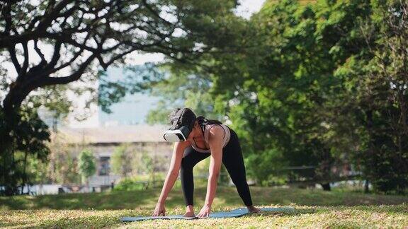 亚洲运动女性戴着虚拟现实眼镜在公园做瑜伽和锻炼