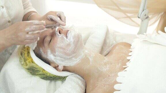 美容师在美容院用餐巾擦拭女人脸上的白泥面膜