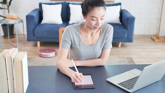 亚洲年轻女子使用数字平板电脑在家在线学习新的家庭办公室设置