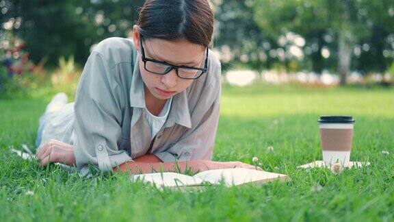 一个十几岁的女学生躺在户外读书回到学校梦想灵感女学生在大学院子或公园的草地上看书远程学习