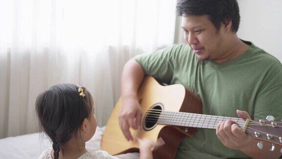 幸福的家庭在家里用乐器享受父亲和女儿一起玩吉他