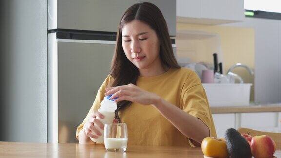 年轻的亚洲妇女在家里的厨房喝牛奶健康的生活方式