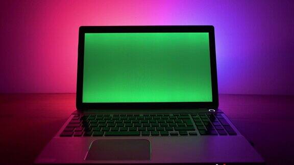 绿色屏幕的笔记本电脑后面有霓虹灯绿色屏幕笔记本站在桌子上