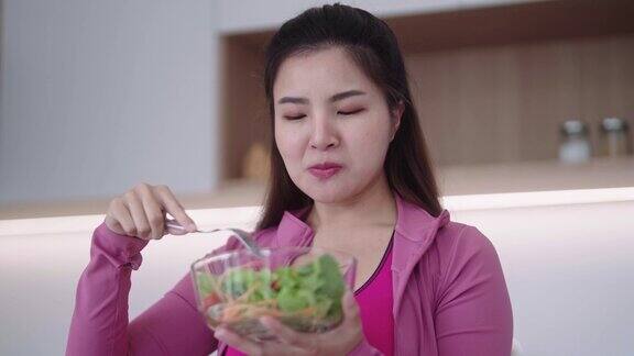 运动的年轻亚洲女性穿着运动服拿着沙拉碗在锻炼后吃健康的新鲜蔬菜沙拉保持减肥饮食和健康食品