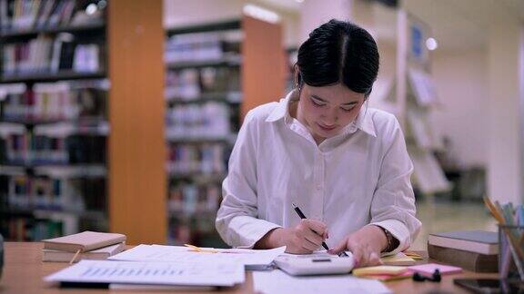 年轻的亚洲女学生在学校图书馆用计算器计算做财务会计作业数学
