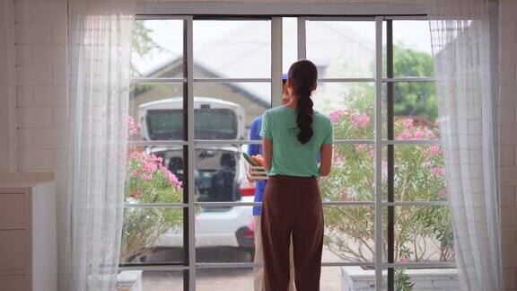 亚洲年轻的快递员在家里给女顾客送包裹穿着蓝色制服的迷人邮递员正在工作把一盒水果和蔬菜杂货送到家门口的女人面前
