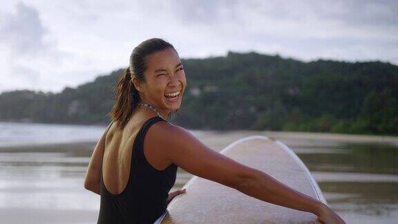 4K肖像的亚洲女子在夏天的夕阳下手持冲浪板行走在热带海滩
