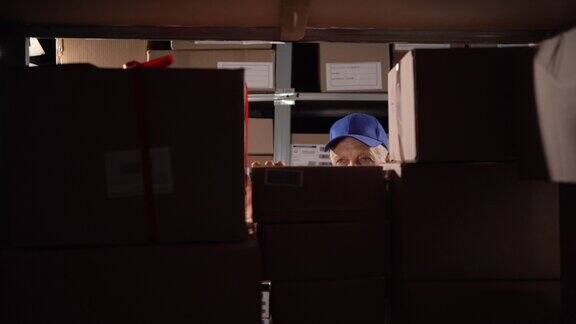 一位年长的仓库工人正在储藏室的架子上找一个纸板箱