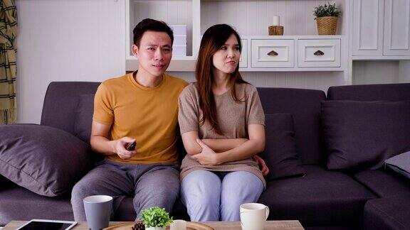 一对年轻的亚洲夫妇在起居室看电视为了抢遥控器而打架