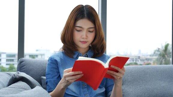 放松的亚洲女人坐在客厅的沙发上看书拿着书看少妇放松读书人翻开书休闲心灵幸福美女人笑脸幸福时光