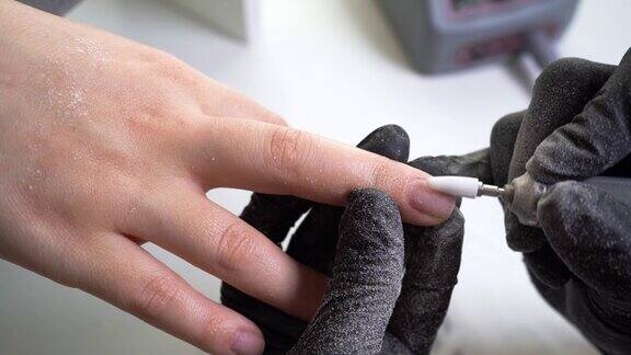在美容院修指甲戴着黑色手套的美甲师用电钻清理女性指甲上的旧指甲油