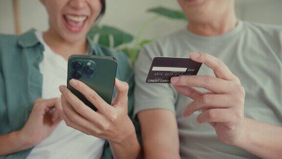 幸福的亚洲夫妇的特写他们一起坐在家里客厅的沙发上玩智能手机购物使用信用卡在线支付生活方式花时间在家里